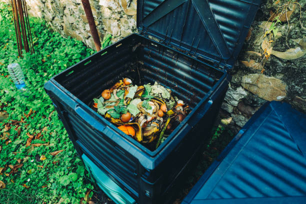 A black compost bin filled with various organic waste sits in a garden, demonstrating composting techniques.